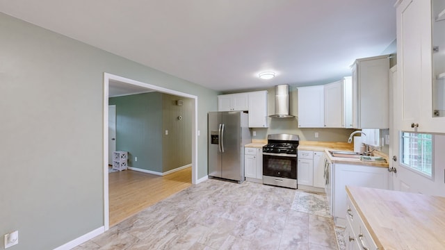 kitchen featuring sink, wall chimney exhaust hood, white cabinetry, butcher block counters, and stainless steel appliances