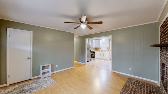 unfurnished living room with ornamental molding, ceiling fan, sink, light hardwood / wood-style flooring, and a fireplace