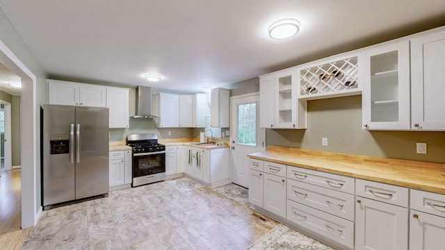 kitchen with white cabinets, appliances with stainless steel finishes, sink, and wall chimney range hood