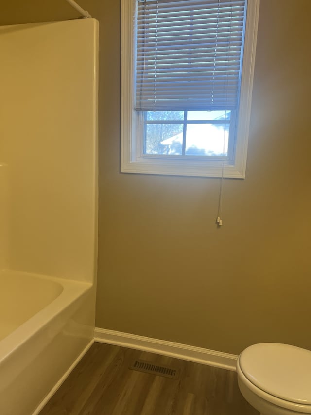 bathroom with a bathing tub, toilet, and hardwood / wood-style flooring