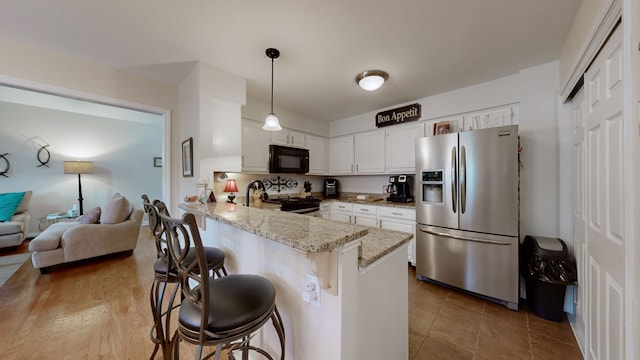 kitchen featuring kitchen peninsula, pendant lighting, a breakfast bar, white cabinets, and black appliances