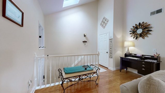 sitting room with light hardwood / wood-style floors, high vaulted ceiling, and a skylight