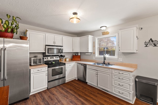 kitchen with appliances with stainless steel finishes, dark hardwood / wood-style flooring, a textured ceiling, sink, and white cabinetry