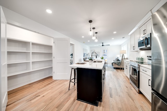 kitchen featuring a kitchen island with sink, white cabinets, hanging light fixtures, ceiling fan, and appliances with stainless steel finishes