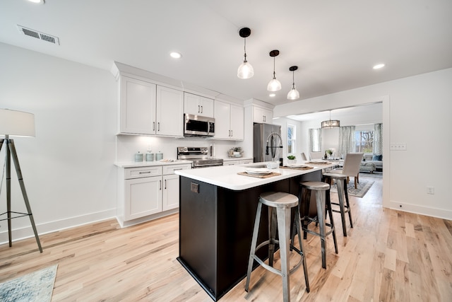 kitchen featuring hanging light fixtures, stainless steel appliances, a center island with sink, white cabinets, and light wood-type flooring