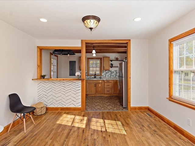 interior space featuring sink, tasteful backsplash, decorative light fixtures, light wood-type flooring, and stainless steel fridge