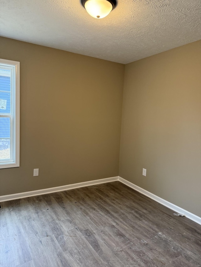 spare room with a textured ceiling, baseboards, and dark wood-type flooring