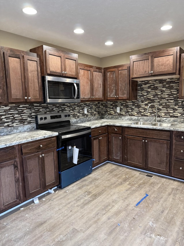 kitchen featuring stainless steel appliances, a sink, light stone countertops, light wood finished floors, and tasteful backsplash