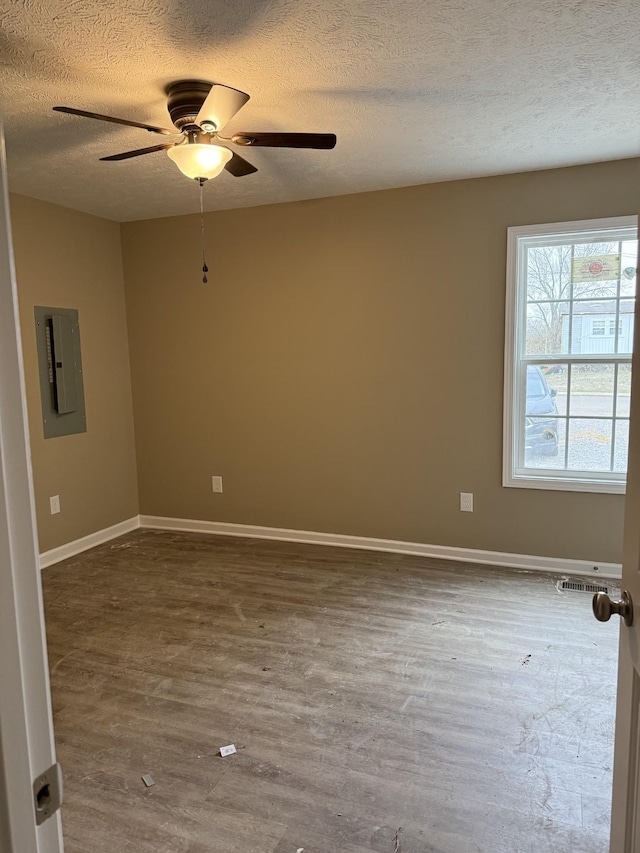 spare room featuring electric panel, baseboards, a ceiling fan, wood finished floors, and a textured ceiling