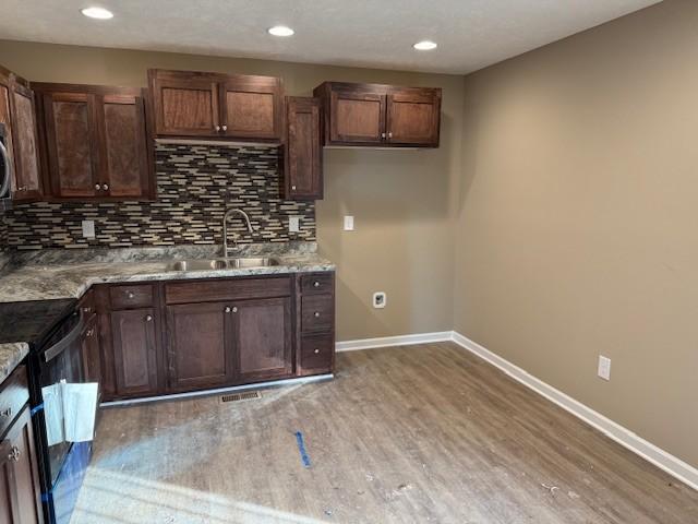 kitchen with baseboards, a sink, decorative backsplash, black range with electric stovetop, and light wood-type flooring