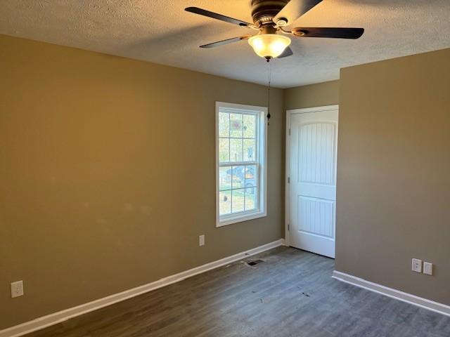 unfurnished room featuring dark wood finished floors, a textured ceiling, baseboards, and ceiling fan