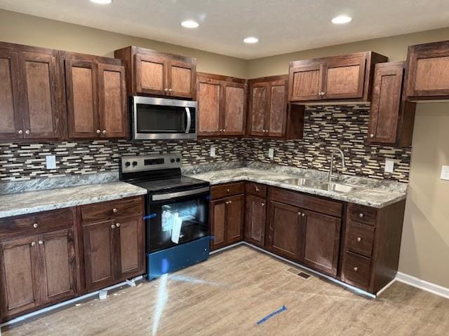 kitchen with light stone countertops, light wood finished floors, a sink, decorative backsplash, and appliances with stainless steel finishes