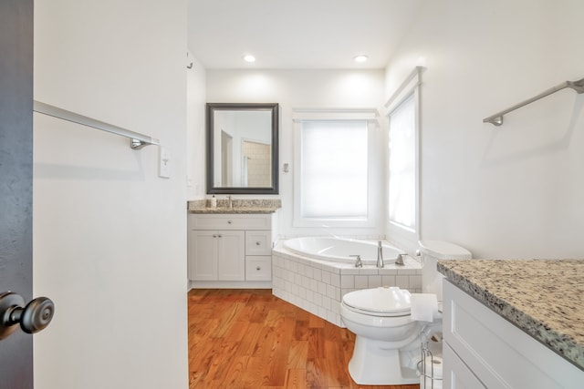 bathroom featuring vanity, a relaxing tiled tub, toilet, and wood-type flooring