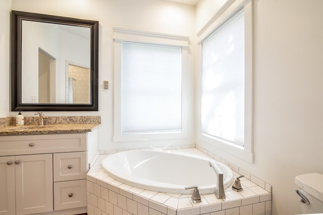 bathroom featuring vanity, a relaxing tiled tub, and toilet