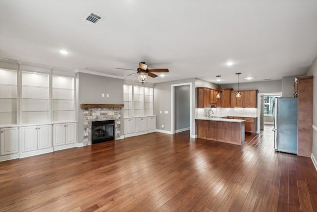 unfurnished living room featuring a stone fireplace, sink, ceiling fan, ornamental molding, and dark hardwood / wood-style flooring