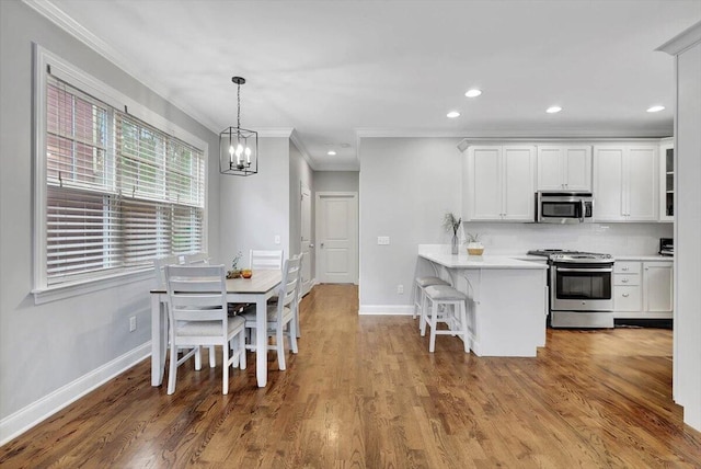 kitchen with kitchen peninsula, appliances with stainless steel finishes, crown molding, light hardwood / wood-style flooring, and white cabinets