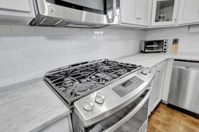 kitchen with light stone countertops, light wood-type flooring, backsplash, stainless steel appliances, and white cabinets