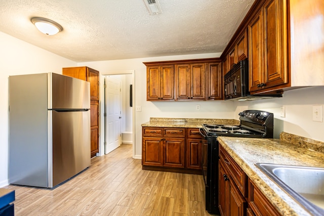 kitchen featuring light stone counters, black appliances, a textured ceiling, and light hardwood / wood-style floors