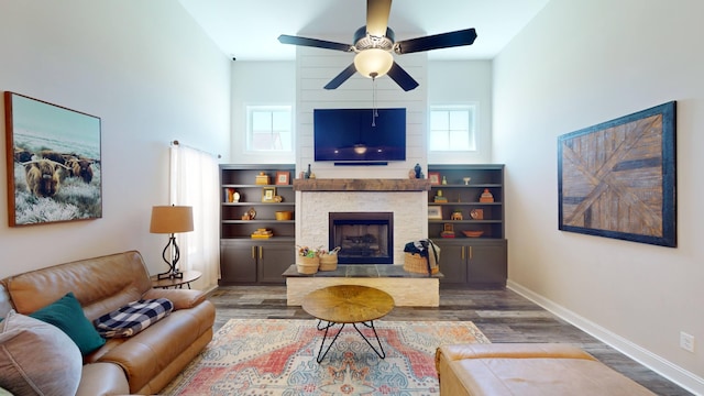 living area featuring ceiling fan, a fireplace, wood finished floors, a towering ceiling, and baseboards