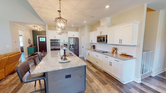 kitchen with stainless steel appliances, a breakfast bar, wood finished floors, white cabinets, and backsplash