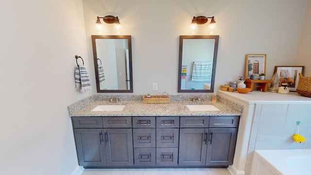 full bath featuring double vanity, a sink, a bathing tub, and baseboards