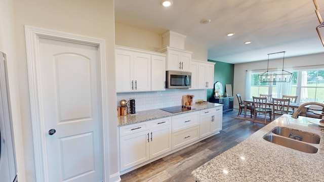 kitchen featuring stainless steel microwave, a sink, black electric cooktop, and white cabinetry