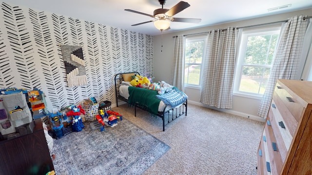 bedroom featuring ceiling fan, light colored carpet, an accent wall, visible vents, and baseboards