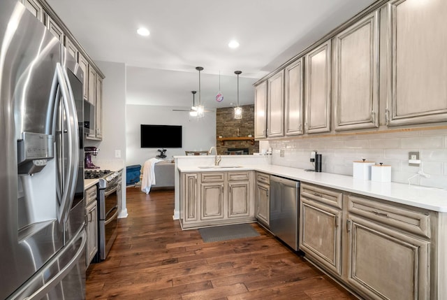 kitchen with sink, dark hardwood / wood-style floors, kitchen peninsula, pendant lighting, and appliances with stainless steel finishes