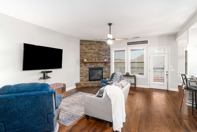 living room with dark hardwood / wood-style flooring, a stone fireplace, and ceiling fan