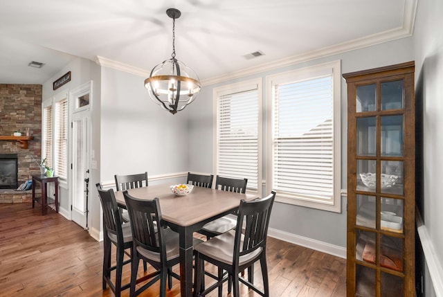 dining area featuring a chandelier, ornamental molding, a stone fireplace, and dark wood-type flooring