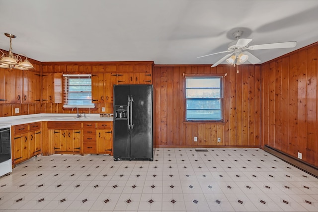 kitchen with pendant lighting, ceiling fan with notable chandelier, black refrigerator with ice dispenser, and wooden walls