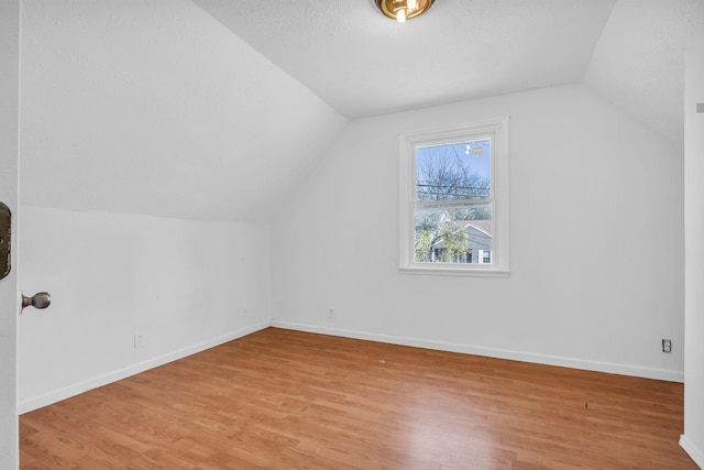 additional living space featuring a textured ceiling, light hardwood / wood-style floors, and lofted ceiling