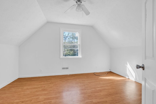 additional living space with a textured ceiling, lofted ceiling, and light wood-type flooring