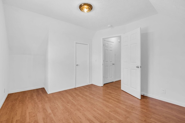 unfurnished bedroom with a textured ceiling, light wood-type flooring, and lofted ceiling