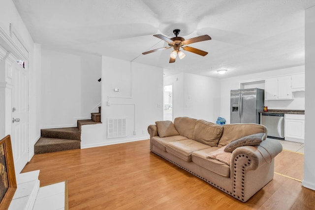 living room with a textured ceiling, light wood-type flooring, and ceiling fan