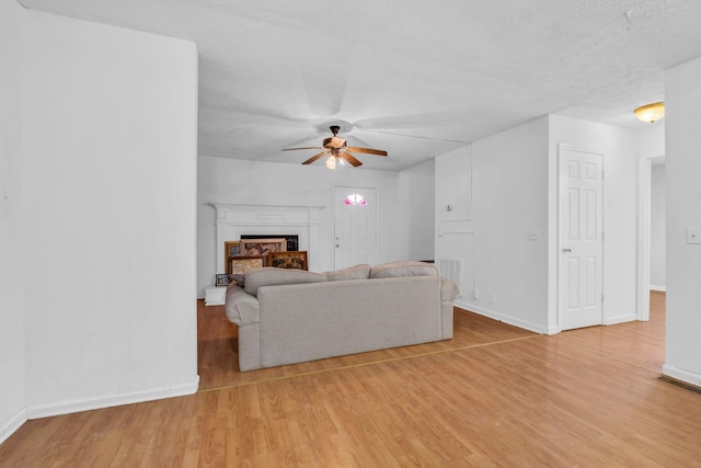 living room featuring ceiling fan, light wood-type flooring, and a textured ceiling