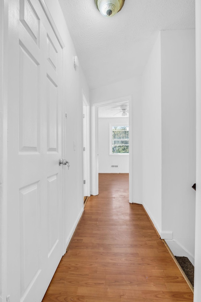 corridor with light wood-type flooring and a textured ceiling