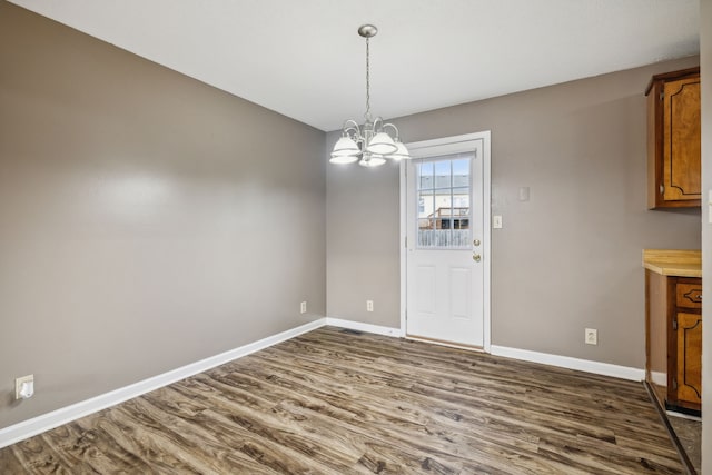 unfurnished dining area with a notable chandelier and dark wood-type flooring