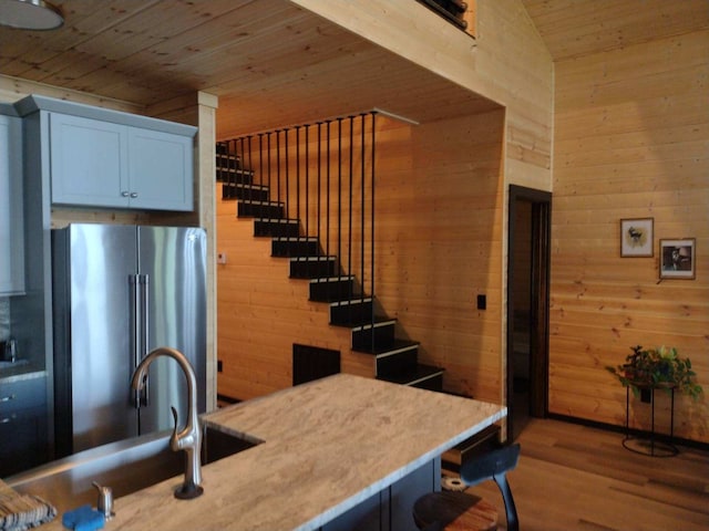 kitchen with stainless steel refrigerator, wood walls, wooden ceiling, and light hardwood / wood-style floors