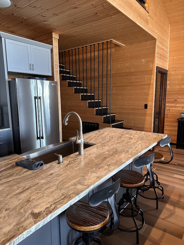 kitchen featuring white cabinetry, stainless steel refrigerator, wooden walls, and wooden ceiling