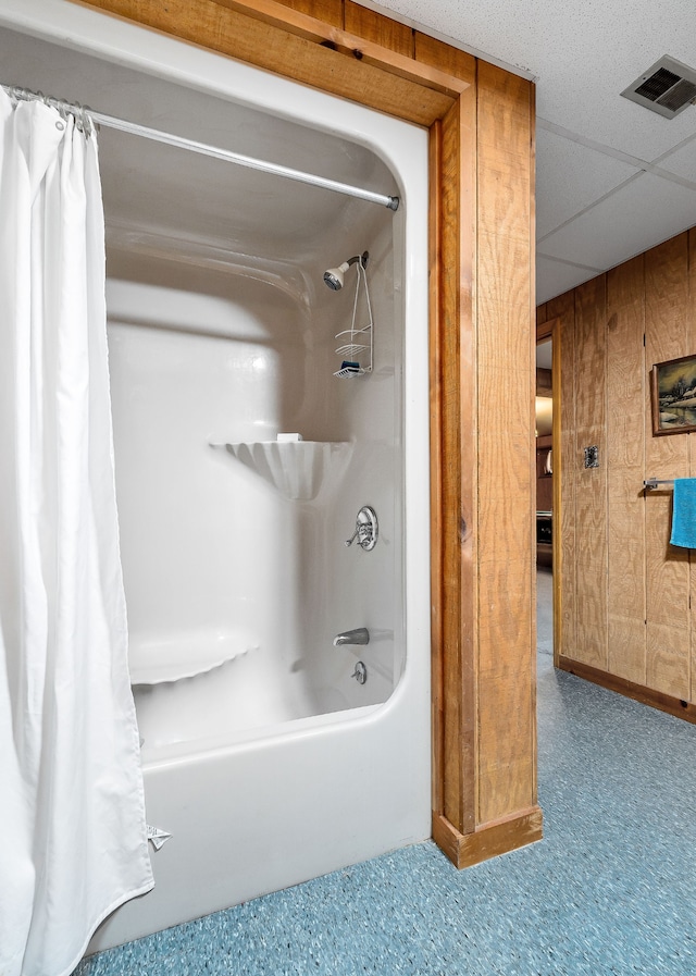 bathroom featuring a paneled ceiling, wood walls, and shower / bath combination with curtain