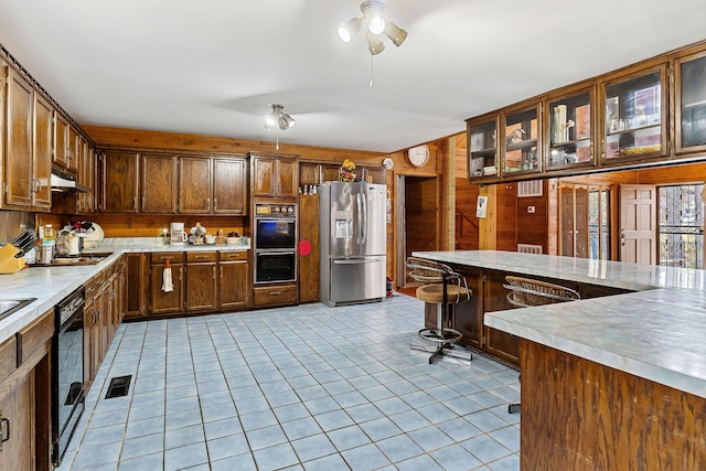 kitchen with black appliances, light tile patterned flooring, and wooden walls