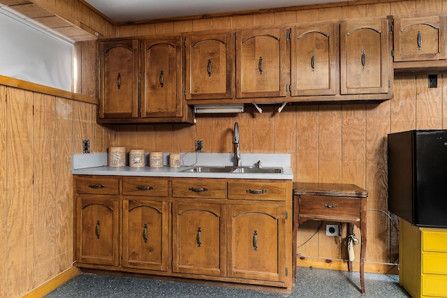 kitchen featuring black refrigerator, wood walls, and sink