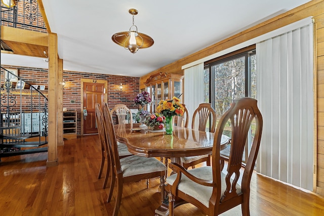 dining area with wood walls, wood-type flooring, and brick wall