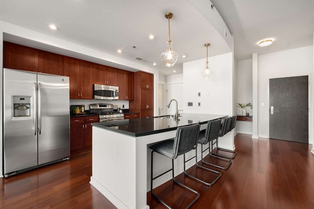 kitchen with appliances with stainless steel finishes, dark wood-type flooring, sink, pendant lighting, and a center island with sink