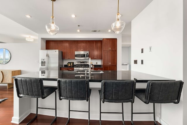 kitchen with a kitchen breakfast bar, hanging light fixtures, dark hardwood / wood-style floors, appliances with stainless steel finishes, and kitchen peninsula