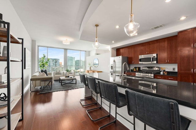 kitchen with sink, dark wood-type flooring, stainless steel appliances, pendant lighting, and a breakfast bar area