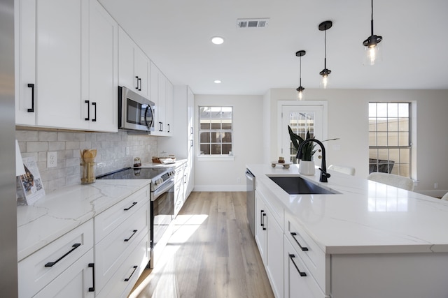 kitchen with a center island with sink, sink, a wealth of natural light, appliances with stainless steel finishes, and decorative light fixtures