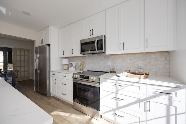 kitchen featuring hardwood / wood-style flooring, white cabinets, light stone countertops, and appliances with stainless steel finishes