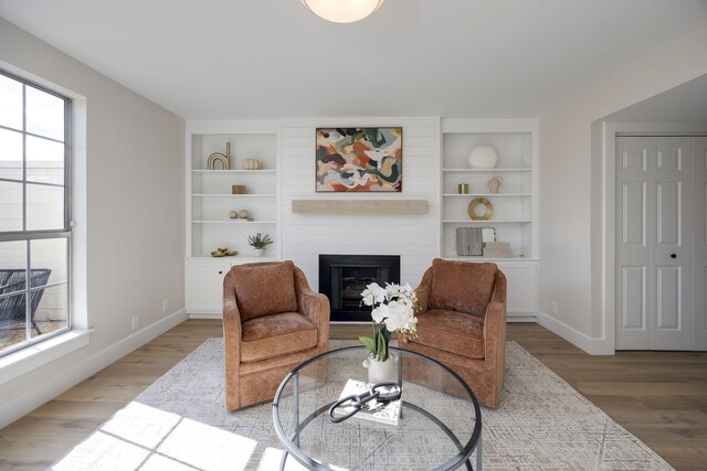 sitting room with hardwood / wood-style flooring, built in shelves, and a large fireplace